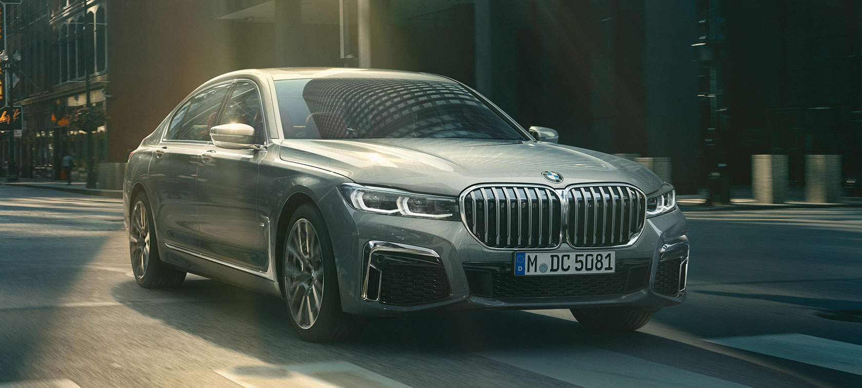 BMW Serie 7 Sedán Gris en movimiento a través de un escenario urbano en vista frontal de tres cuartos