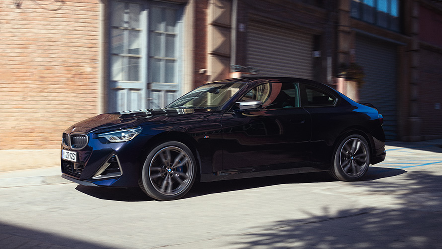 BMW M240i xDrive Coupé G42 2021 Vista del lateral, parado BMW M240i xDrive Coupé G42 2021 Black Sapphire metalizado Vista del lateral, parado delante de un almacén