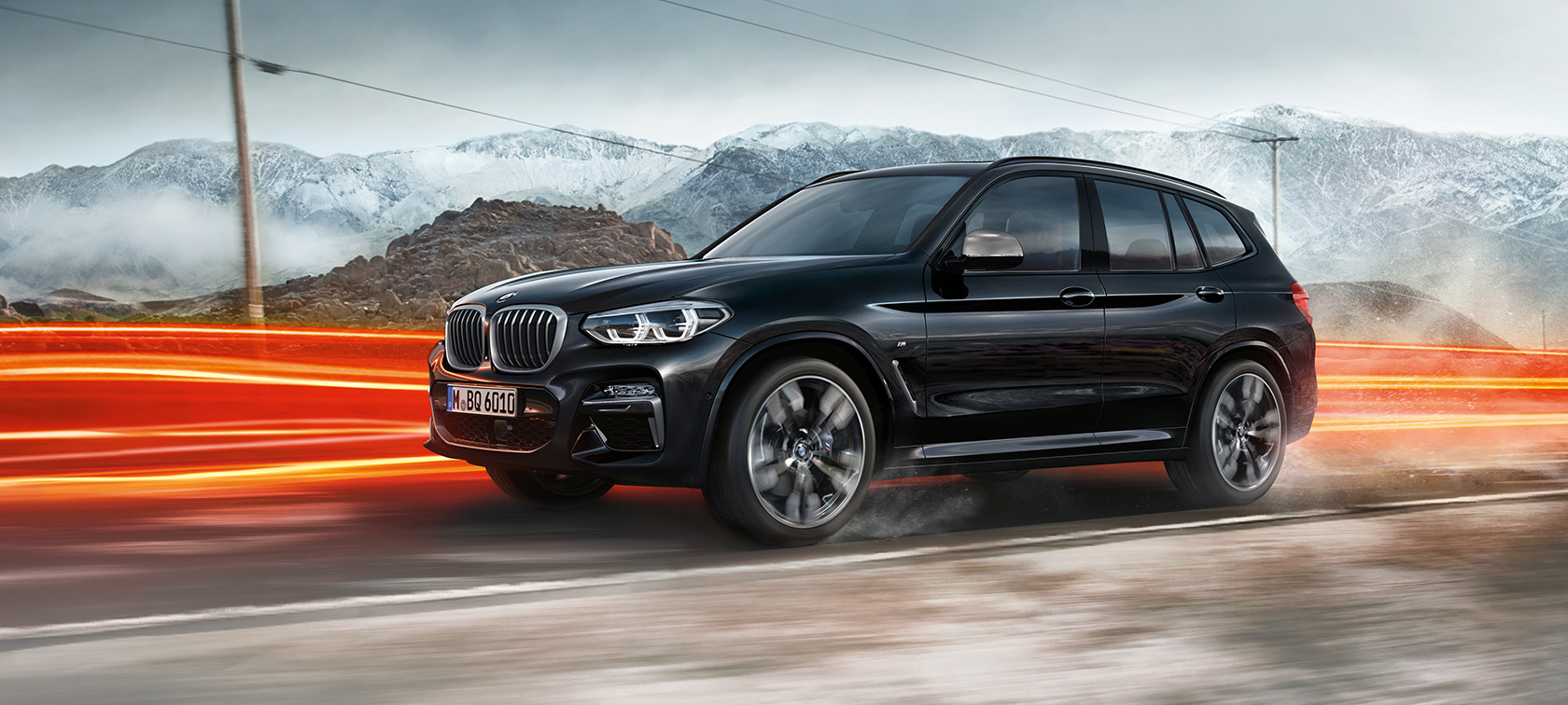 BMW X3 M40i y BMW X3 M40d, vista lateral. BMW X3 M40i y BMW X3 M40d en Black Sapphire metálico, en movimiento, exterior, vista lateral frente a un paisaje montañoso con franjas de luz.