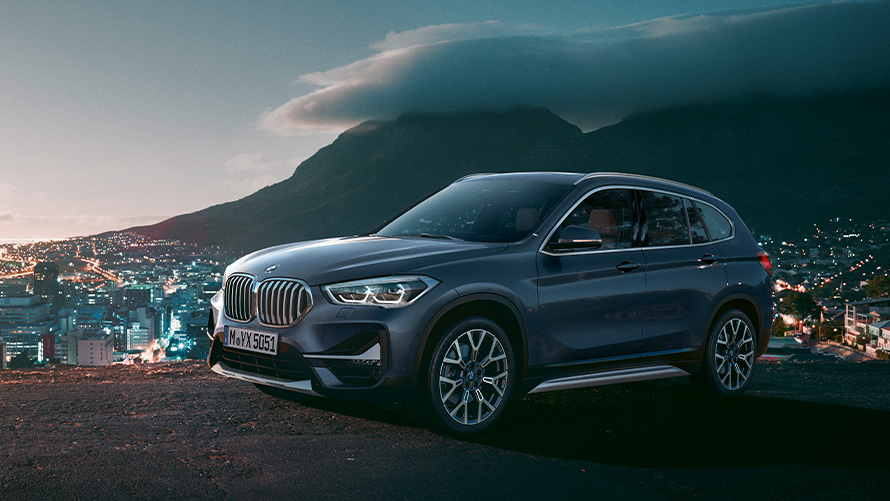 BMW X1 F48, segunda generación, vista de tres cuartos del lateral, parado delante de una ciudad Modelos BMW X BMW X1 F48, segunda generación, vista de tres cuartos del lateral, parado delante de una ciudad