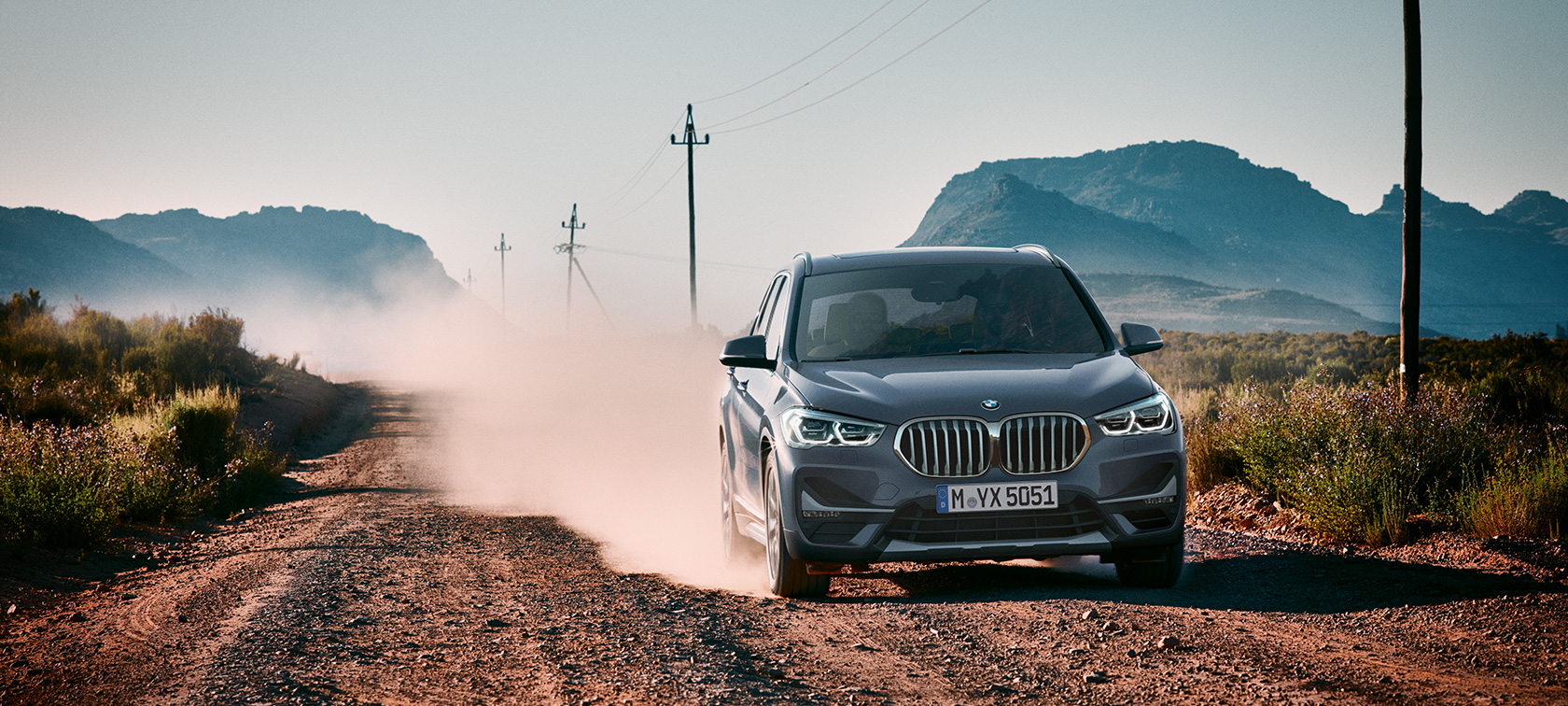 BMW X1, vista trasera tres cuartos. BMW X1, vista trasera tres cuartos frente a un escenario todo terreno.