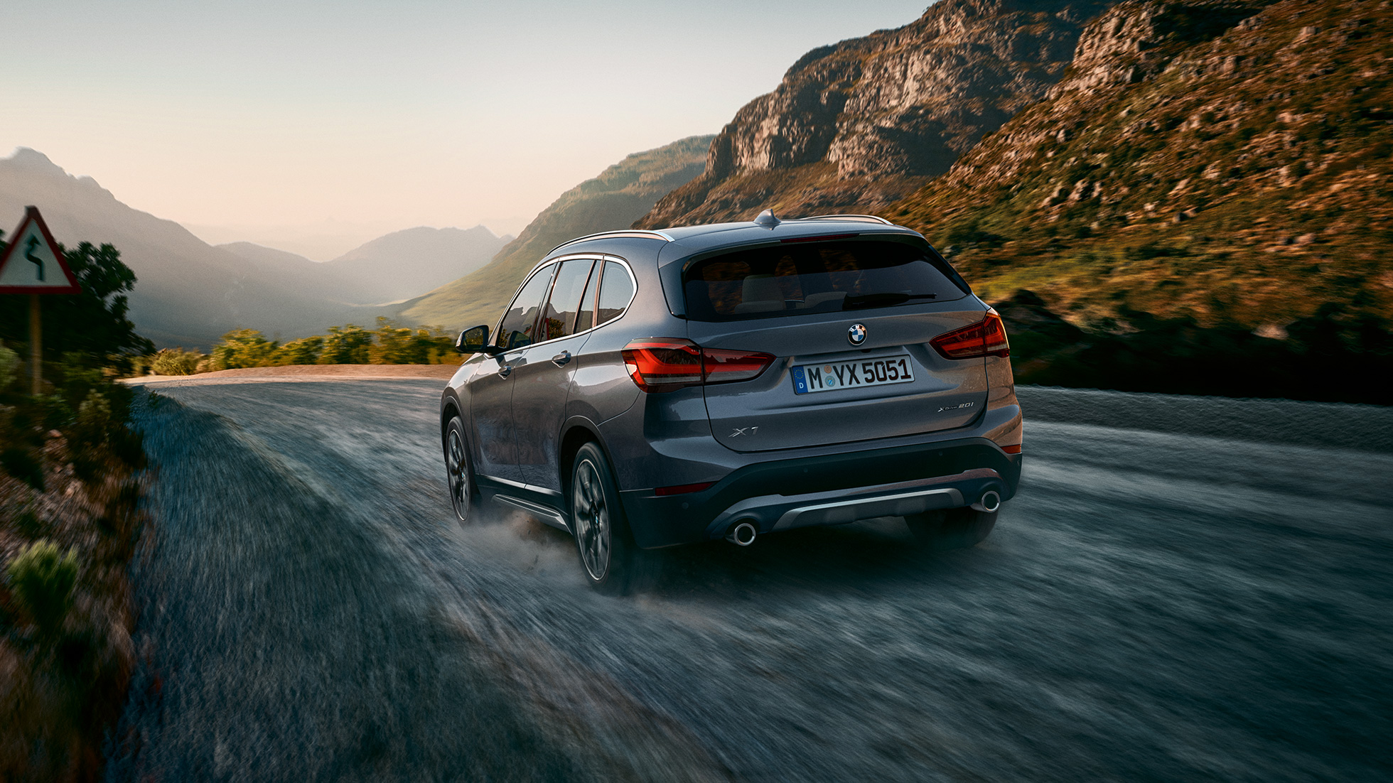 BMW X1, vista trasera tres cuartos. BMW X1, vista trasera tres cuartos frente a un escenario todo terreno.