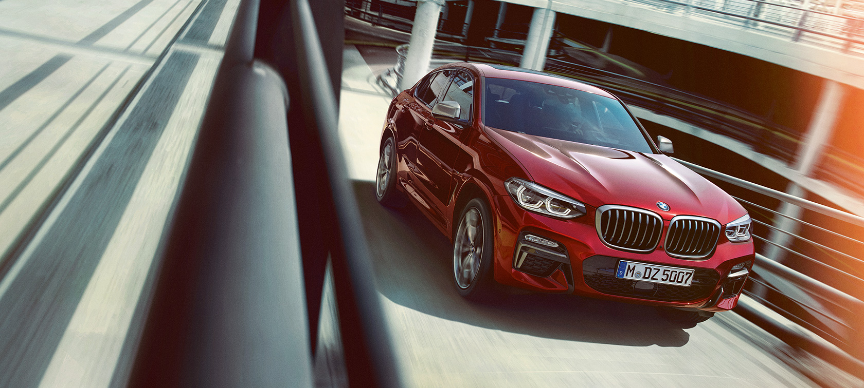 BMW X4 en movimiento en el estacionamiento Vista lateral de tres cuartos del BMW X4 2018 Flamenco Red efecto brillante en movimiento en el estacionamiento