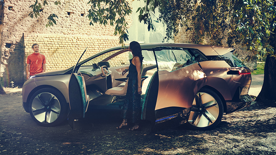 Vista lateral BMW Vision iNEXT Vista lateral BMW Vision iNEXT con mujer en puertas abiertas y hombre en el fondo