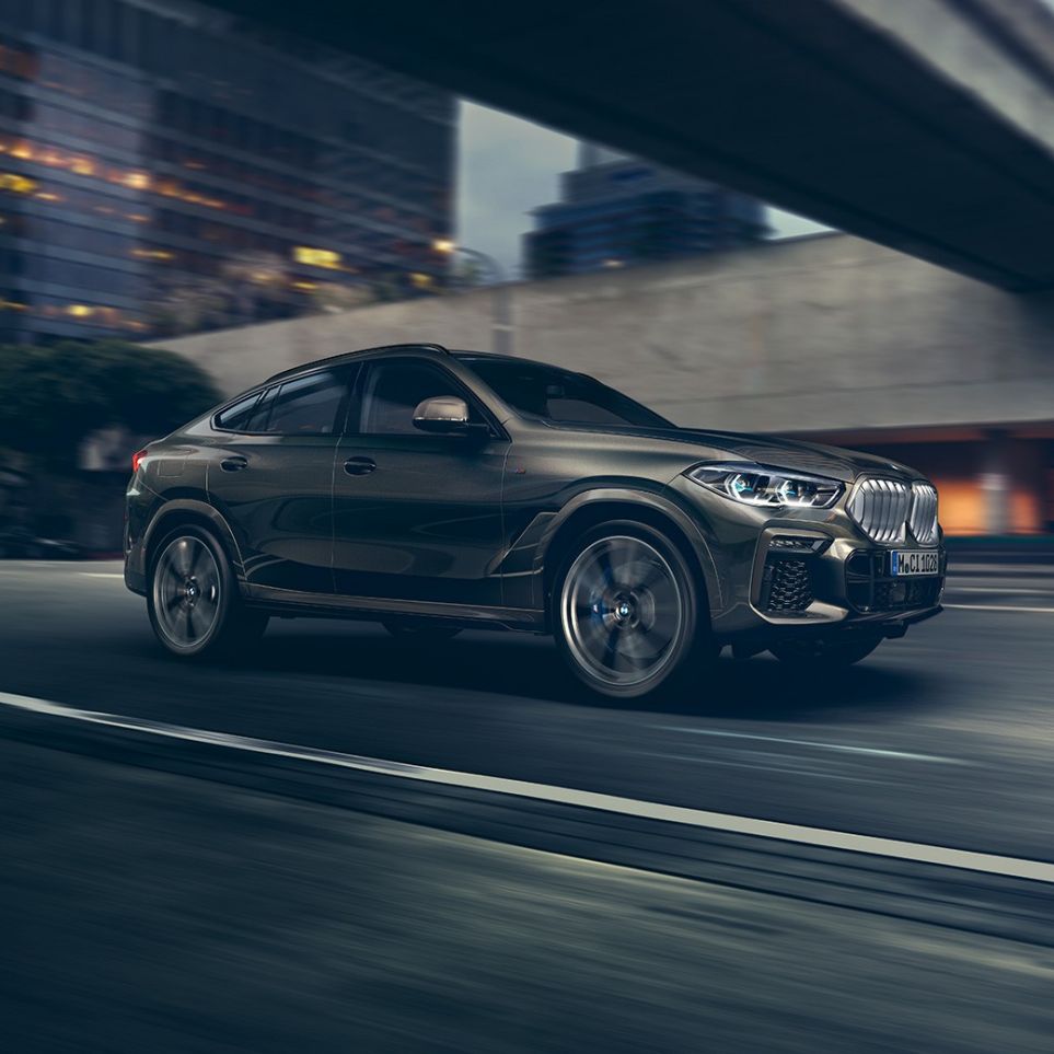 Conducción del BMW X6. BMW X6 en perspectiva frontal de tres cuartos en movimiento frente a un escenario urbano.